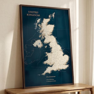 May include: A framed wall map of the United Kingdom featuring a deep blue background and a cream-coloured landmass with detailed geography. The text reads United Kingdom, Our Adventures, Past Adventures, and Adventures to Come in gold lettering.