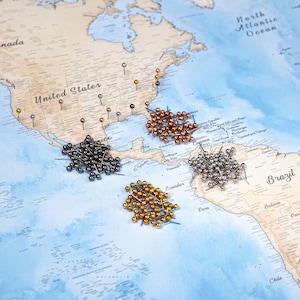 May include: A world map with push pins marking locations. The pins are in various metallic colors, including gold, copper, silver, and black. The map shows the United States, South America, and the Atlantic Ocean.