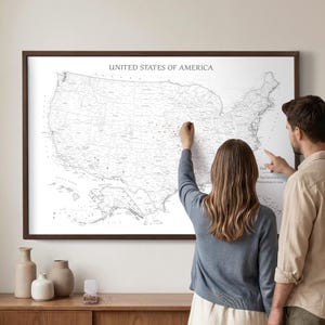 May include: A large framed wall map of the United States of America with a white background and black text. The map displays state borders, cities, and geographic features. The title UNITED STATES OF AMERICA is printed in black at the top center.