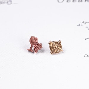 May include: Two small metal pins. One pin is a copper-coloured wine glass paired with a cluster of grapes. The second pin is a gold-coloured circular plate featuring a crossed fork and knife design. Both items are detailed with embossed textures.