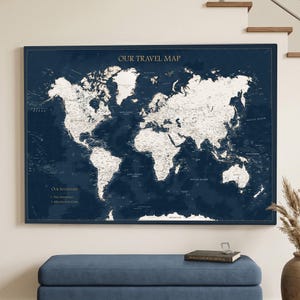 Könnte beinhalten: Eine rechteckige Wandkarte mit dem Titel OUR TRAVEL MAP, die einen dunkelblauen Hintergrund mit weißen Kontinenten und Ozeanen aufweist. Die Karte enthält Textbeschriftungen für Länder und Ozeane sowie eine Legende in der unteren linken Ecke.