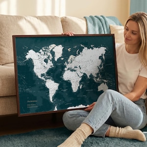 Può includere: Una mappa del mondo incorniciata con uno sfondo verde acqua scuro e masse terrestri bianche. La mappa presenta il testo "Our Adventures" nell'angolo in basso a sinistra, seguito da due righe di testo parzialmente oscurate.