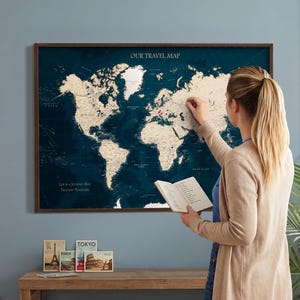 Op de afbeelding: Een wereldkaart met een donkerblauwe achtergrond en een houten frame. De kaart heeft een vintage uitstraling met beige landmassa's en de tekst "Our Travel Map" en "Life is a Journey Best Traveled Together".