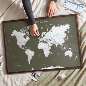 Puede incluir: Un mapa del mundo enmarcado con un fondo verde oliva oscuro y masas terrestres blancas. El texto "World Travel Map" aparece en la parte superior, con "Our Travels" y "Past Adventures" y "Adventures to Come" impresos en la esquina inferior izquierda.
