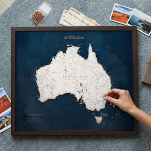 May include: A framed map of Australia with a dark blue background and a light-colored landmass featuring detailed topography. The map includes the text "AUSTRALIA" and a legend labeled "Our Adventures" with "Past Adventures" and "Adventures to Come".