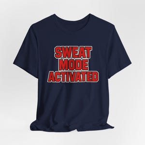 May include: Navy blue t-shirt with the text "SWEAT MODE ACTIVATED" in red letters with a white outline. The shirt is a crew neck style and appears to be made of a soft material.