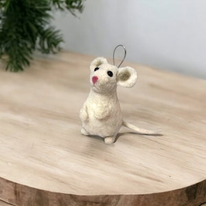 May include: A white felt mouse ornament with black eyes and a pink nose. The mouse has a wire loop for hanging.
