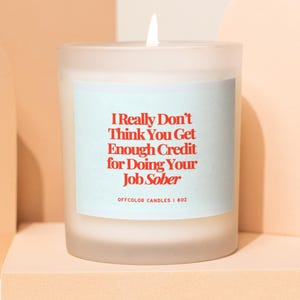 Può includere: Una candela in vetro smerigliato bianco con uno stoppino acceso. La candela ha un'etichetta azzurra con testo rosso che recita "I Really Don't Think You Get Enough Credit for Doing Your Job Sober." Il testo "OFFCOLOR CANDLES I 8OZ" è sotto.