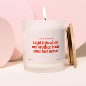 May include: A lit white candle in a frosted glass jar with a wooden lid. The label reads "DEAR SARAH, Light this when my brother is on your last nerve." The candle is 4 oz (113 g).