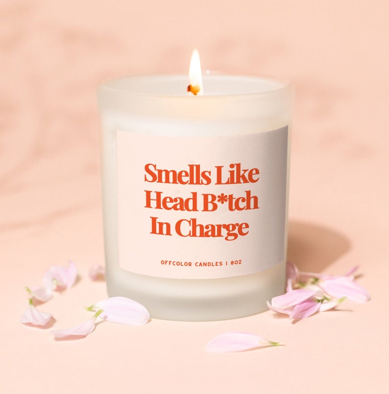 Może przedstawiać: Biała, matowa świeca w szklanym naczyniu z białą etykietą, na kt&oacute;rej widnieje napis "Smells Like Head B*tch In Charge" oraz "Offcolor Candles | 8oz".