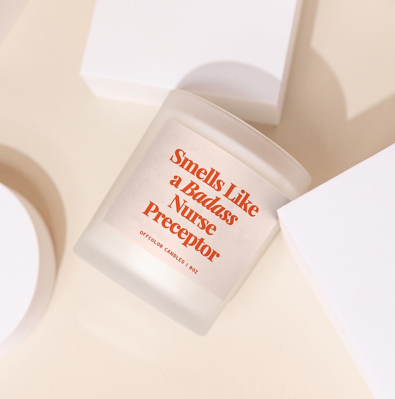 May include: A white candle with a red label that reads "Smells Like a Badass Nurse Preceptor" and "Offcolor Candles | 8oz".