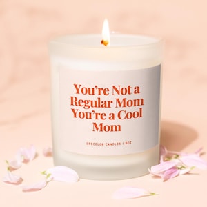 Puede incluir: Vela blanca en un tarro de vidrio esmerilado con una etiqueta que dice "You're Not a Regular Mom You're a Cool Mom" con el texto en naranja. La etiqueta tambi&eacute;n dice "Offcolor Candles | 8oz".