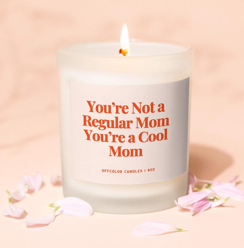 Puede incluir: Vela blanca en un tarro de vidrio esmerilado con una etiqueta que dice "You're Not a Regular Mom You're a Cool Mom" con el texto en naranja. La etiqueta tambi&eacute;n dice "Offcolor Candles | 8oz".