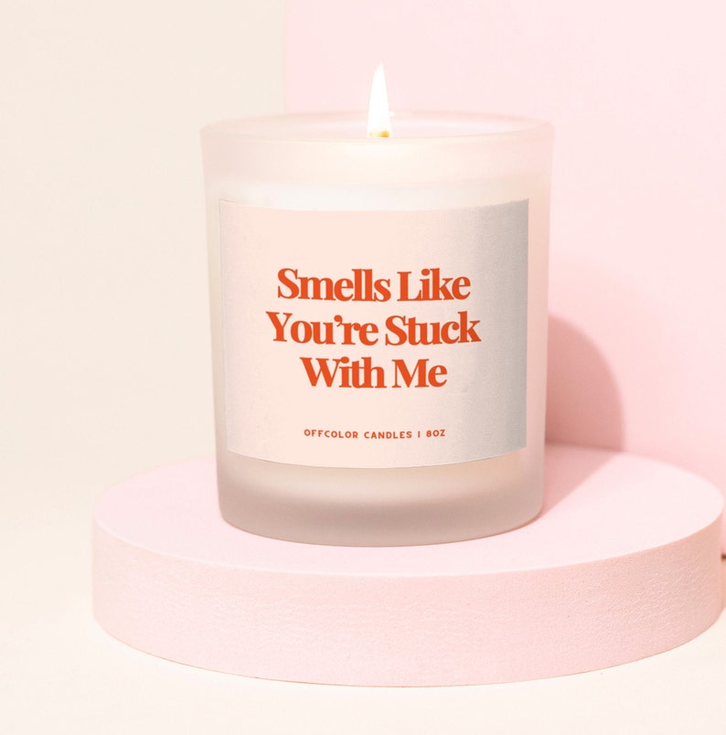 A clear jar candle with a white label with orange text on it