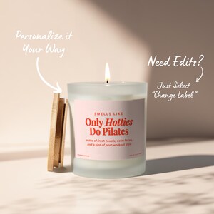May include: A lit candle in a frosted glass jar with a wooden lid. The label reads "Only Hotties Do Pilates" with scent notes. Text on the image says "Personalize it Your Way" and "Need Edits? Just Select 'Change Label'".