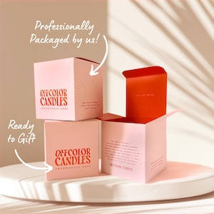 May include: Pink square boxes of Offcolor Candles, stacked on a white surface. The boxes have red text that reads "Offcolor Candles" and "Ready to Gift." One box is open, revealing a red interior. The text "Professionally Packaged by us!" is also visible.