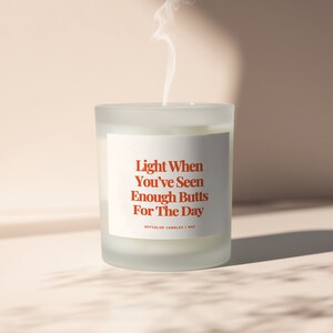 May include: White frosted glass candle with a white label that reads "Light When You've Seen Enough Butts For The Day" in red text. The label also includes the text "Offcolor Candles | 8oz".