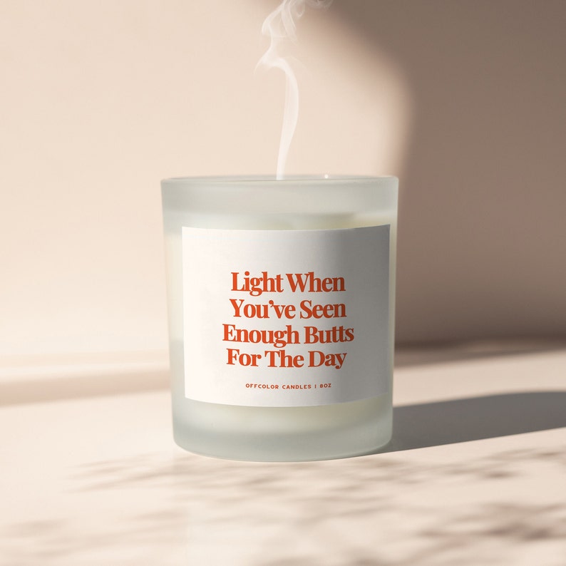 May include: White frosted glass candle with a white label that reads "Light When You've Seen Enough Butts For The Day" in red text. The label also includes the text "Offcolor Candles | 8oz".