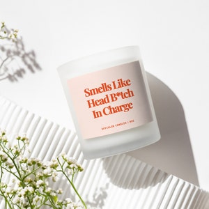 Może przedstawiać: Biała, matowa świeca w szklanym naczyniu z r&oacute;żową etykietą, na kt&oacute;rej widnieje napis "Smells Like Head B*tch In Charge" oraz "OFFCOLOR CANDLES | 8OZ".