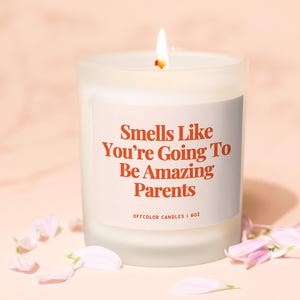 Op de afbeelding: Witte kaars met een label met de tekst "Smells Like You're Going To Be Amazing Parents" en "Offcolor Candles | 8oz".