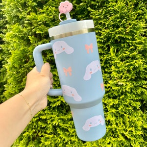 May include: A light blue stainless steel travel mug with a handle and a pink cloud shaped lid. The mug is decorated with a pattern of white cartoon dogs with pink bows.