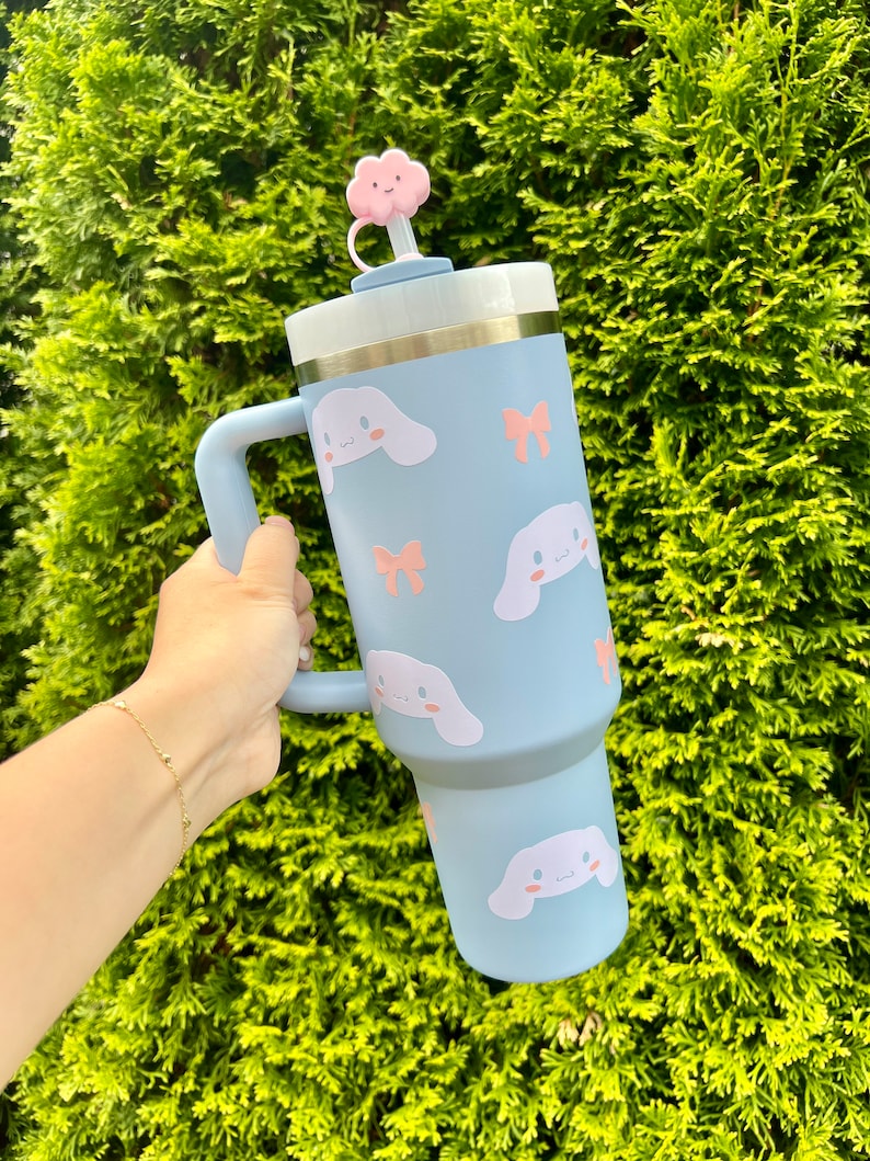 May include: A light blue stainless steel travel mug with a handle and a pink cloud shaped lid. The mug is decorated with a pattern of white cartoon dogs with pink bows.