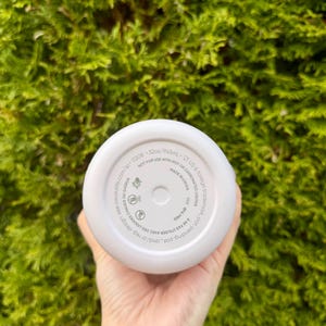 May include: A white insulated water bottle with a 32oz/945mL capacity. The bottom of the bottle has printed text including "NOT FOR USE WITH HOT OR CARBONATED LIQUIDS" and "MADE IN CHINA". The bottle is held in a hand against a green background.