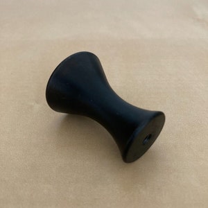 Op de afbeelding: Zwarte kastknop met een afgeronde bovenkant en een licht uitlopende basis.