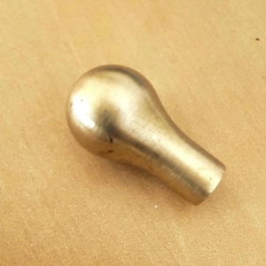 May include: A brass-colored knob with a rounded top and a cylindrical base. The knob has a smooth, polished surface and is likely used for furniture or decorative purposes. The background is a light brown color.