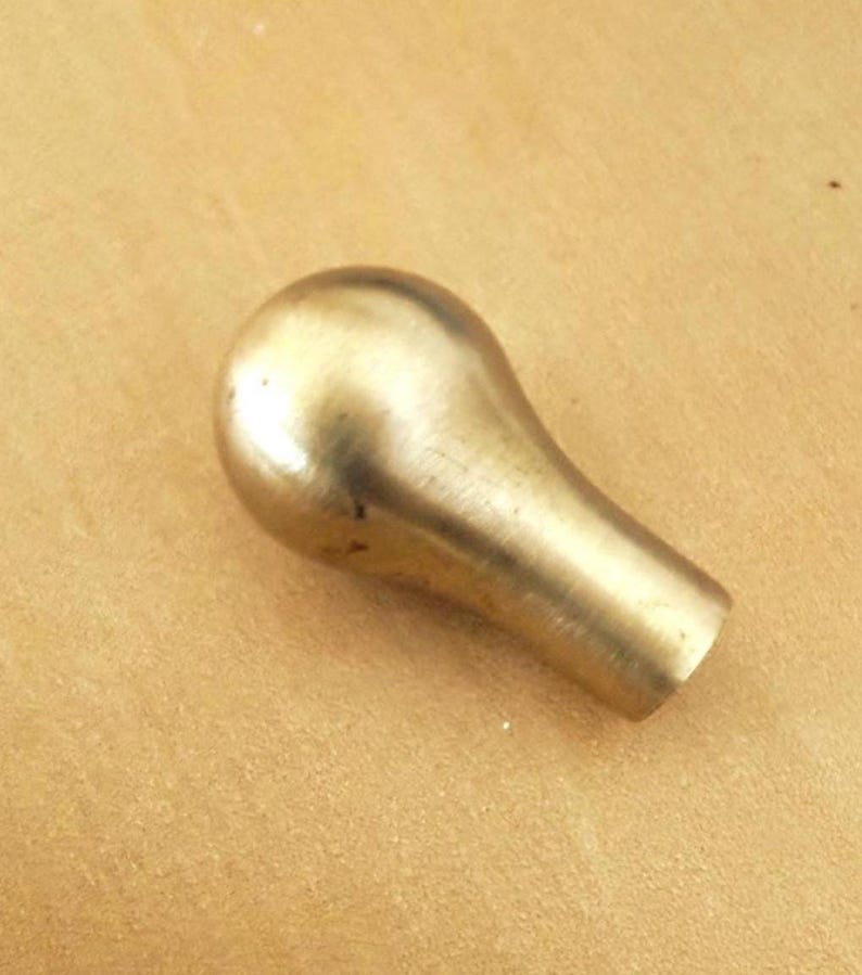 May include: A brass-colored knob with a rounded top and a cylindrical base. The knob has a smooth, polished surface and is likely used for furniture or decorative purposes. The background is a light brown color.
