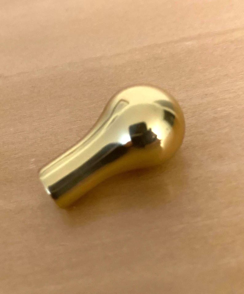 May include: A shiny, gold-colored knob with a rounded top and a tapered base. The knob reflects the surrounding environment, creating a mirrored effect. The smooth surface suggests a decorative or functional item.