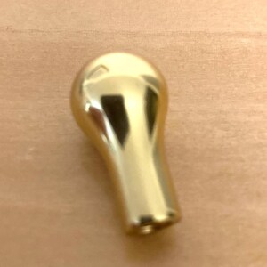 May include: A shiny, gold-colored knob with a rounded top and a tapered, cylindrical base. The knob is made of a reflective material, and it is likely used for furniture or decorative purposes.