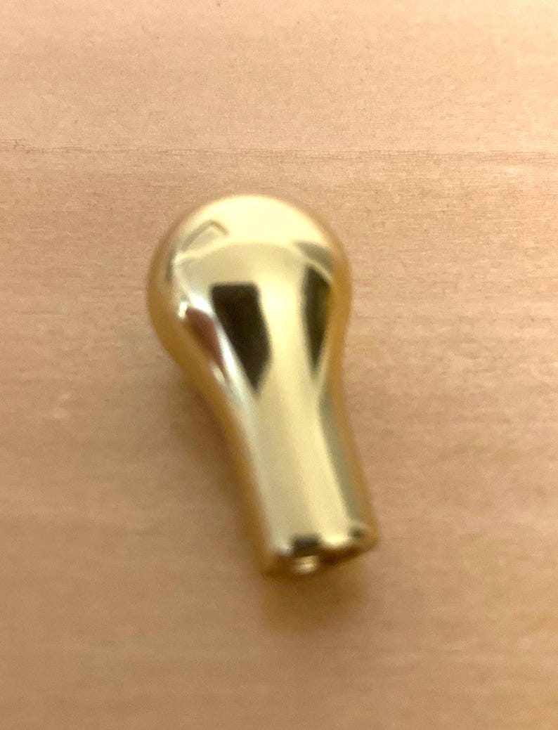 May include: A shiny, gold-colored knob with a rounded top and a tapered, cylindrical base. The knob is made of a reflective material, and it is likely used for furniture or decorative purposes.