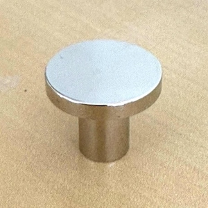 Op de afbeelding: Een zilveren en chromen kastknop met een cilindrische basis en een platte, ronde bovenkant. De knop is gemaakt van metaal en heeft een gepolijste afwerking. De hardware is ontworpen voor gebruik op lades en kasten.