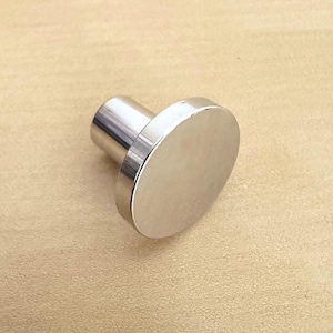 May include: A circular cabinet knob with a polished silver-tone metallic finish. The hardware features a flat, round face connected to a cylindrical base, providing a smooth, reflective surface that catches light across its entire front profile.