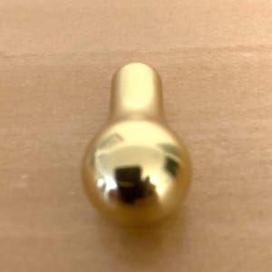May include: A shiny, gold-colored bottle stopper with a rounded base and a cylindrical top. The stopper reflects the surrounding environment, creating a mirrored effect. The design is simple and elegant.