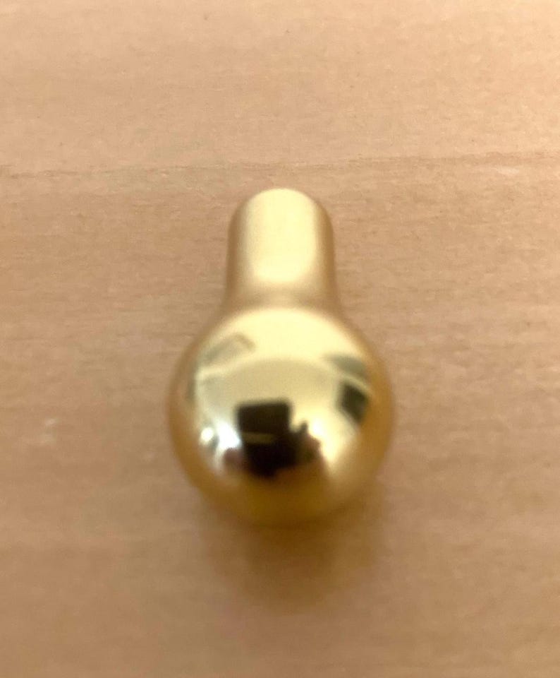 May include: A shiny, gold-colored bottle stopper with a rounded base and a cylindrical top. The stopper reflects the surrounding environment, creating a mirrored effect. The design is simple and elegant.