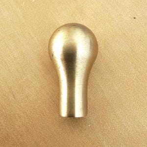May include: A solid brass cabinet knob with a rounded top and a cylindrical base. The knob has a smooth, polished finish and a warm, golden color. This hardware is suitable for drawers and cabinets.
