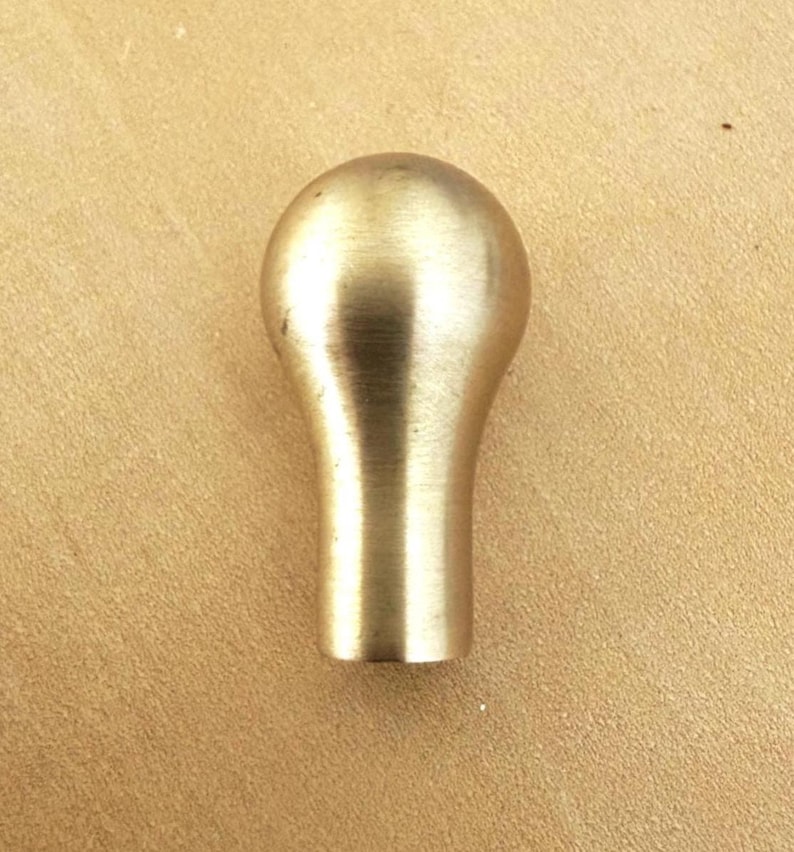 May include: A solid brass cabinet knob with a rounded top and a cylindrical base. The knob has a smooth, polished finish and a warm, golden color. This hardware is suitable for drawers and cabinets.