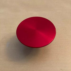 May include: A bright red round button with a smooth, shiny surface.
