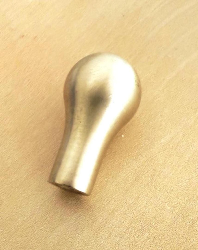 May include: A brass-colored cabinet knob with a rounded top and a tapered base. The knob has a smooth, polished finish and is designed for easy gripping. This hardware is suitable for drawers and cabinets.