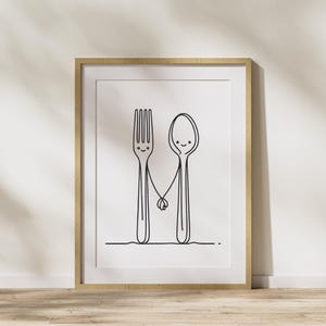 May include: A black and white line drawing of a fork and spoon holding hands. The fork and spoon have smiley faces. The drawing is framed in a light wood frame.