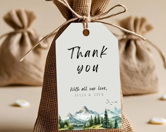 May include: A burlap favor bag with a white tag that reads "Thank you." The tag features a watercolor mountain scene and the names Julia & Jack. The bag is tied with a natural twine bow.