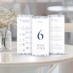 May include: Blue and white wedding table cards with a floral design. The cards include a wedding timeline, table number 6, and a menu for Julia and Jack's wedding on 22.12.2X.