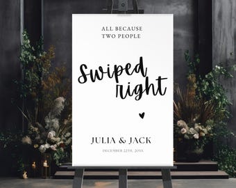 Puede incluir: Un letrero blanco sobre un caballete de madera con el texto "ALL BECAUSE TWO PEOPLE Swiped right" y un símbolo de corazón. Debajo del corazón, el letrero dice "JULIA & JACK" y "DECEMBER 22TH, 20XX". El letrero está rodeado de vegetación.