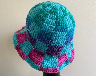 May include: A crocheted bucket hat with a colorful patchwork design. The hat is made with shades of blue, green, purple, and pink yarn.