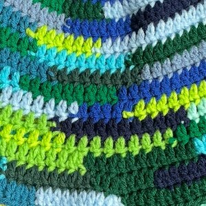 May include: A multi-colored crochet fabric featuring a dense, textured stitch pattern. The yarn displays a vibrant palette of forest green, lime green, bright turquoise, royal blue, navy blue, and pale sky blue arranged in irregular, horizontal stripes.