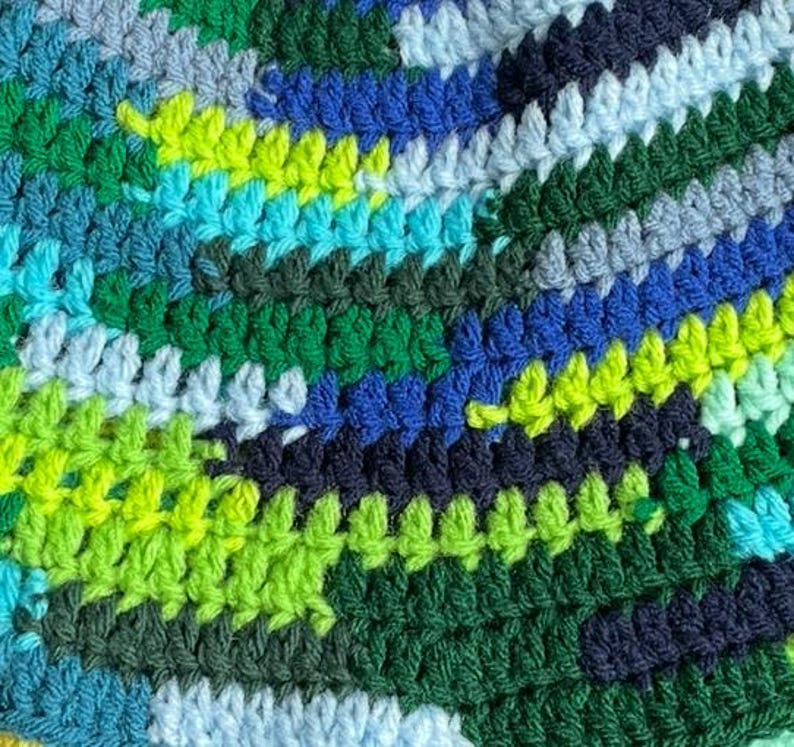May include: A multi-colored crochet fabric featuring a dense, textured stitch pattern. The yarn displays a vibrant palette of forest green, lime green, bright turquoise, royal blue, navy blue, and pale sky blue arranged in irregular, horizontal stripes.