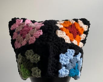 May include: A black crocheted hat with colorful granny squares in pink, orange, red, green, blue, and teal.