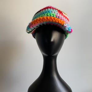 May include: A multi-colored crochet bucket hat featuring a vibrant mix of yarn colors including bright orange, pink, blue, green, and white. The hat has a textured, hand-stitched appearance with a wide, slightly downturned brim and a rounded crown.